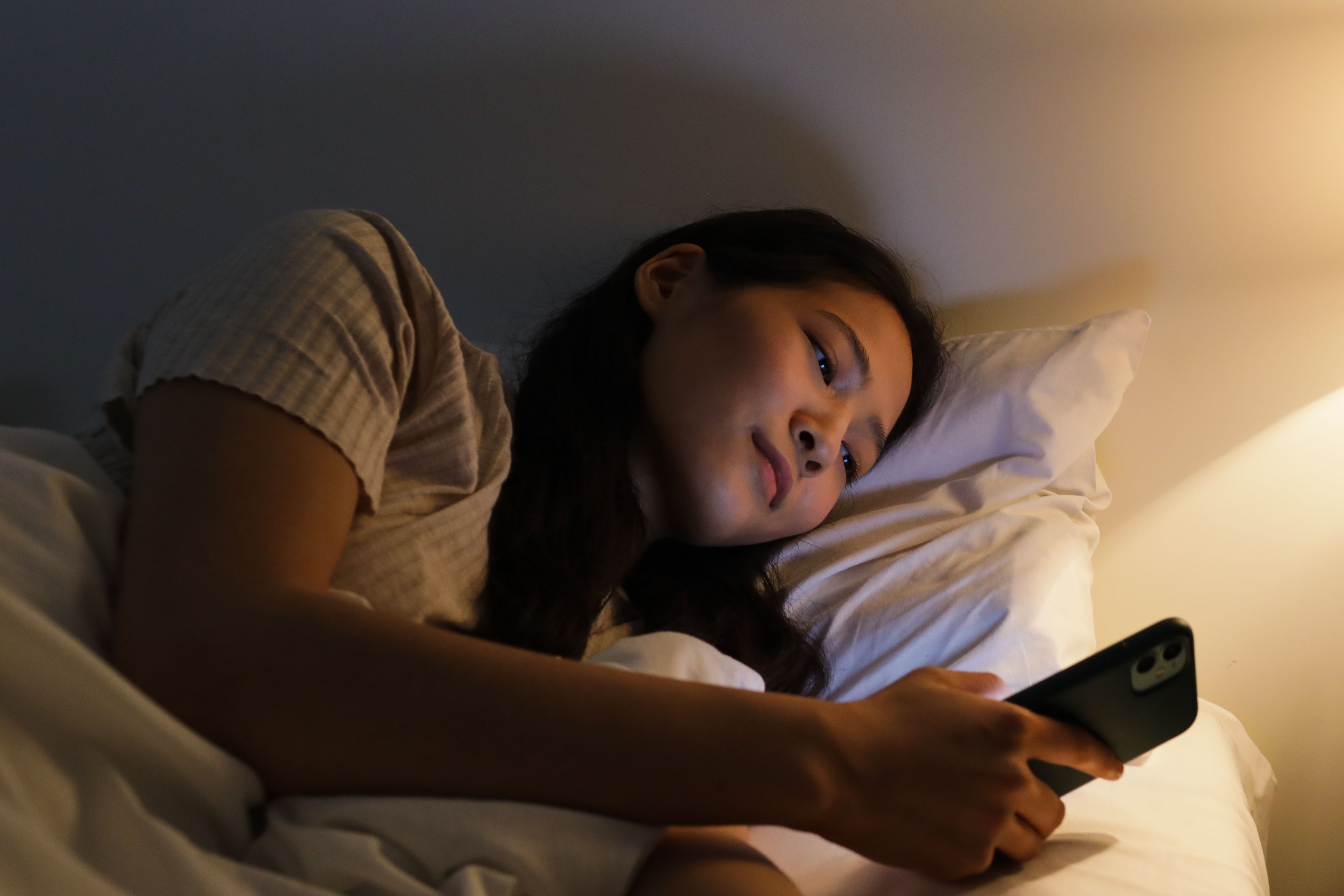 Woman in bed at night messaging on her smartphone in warm bedside light