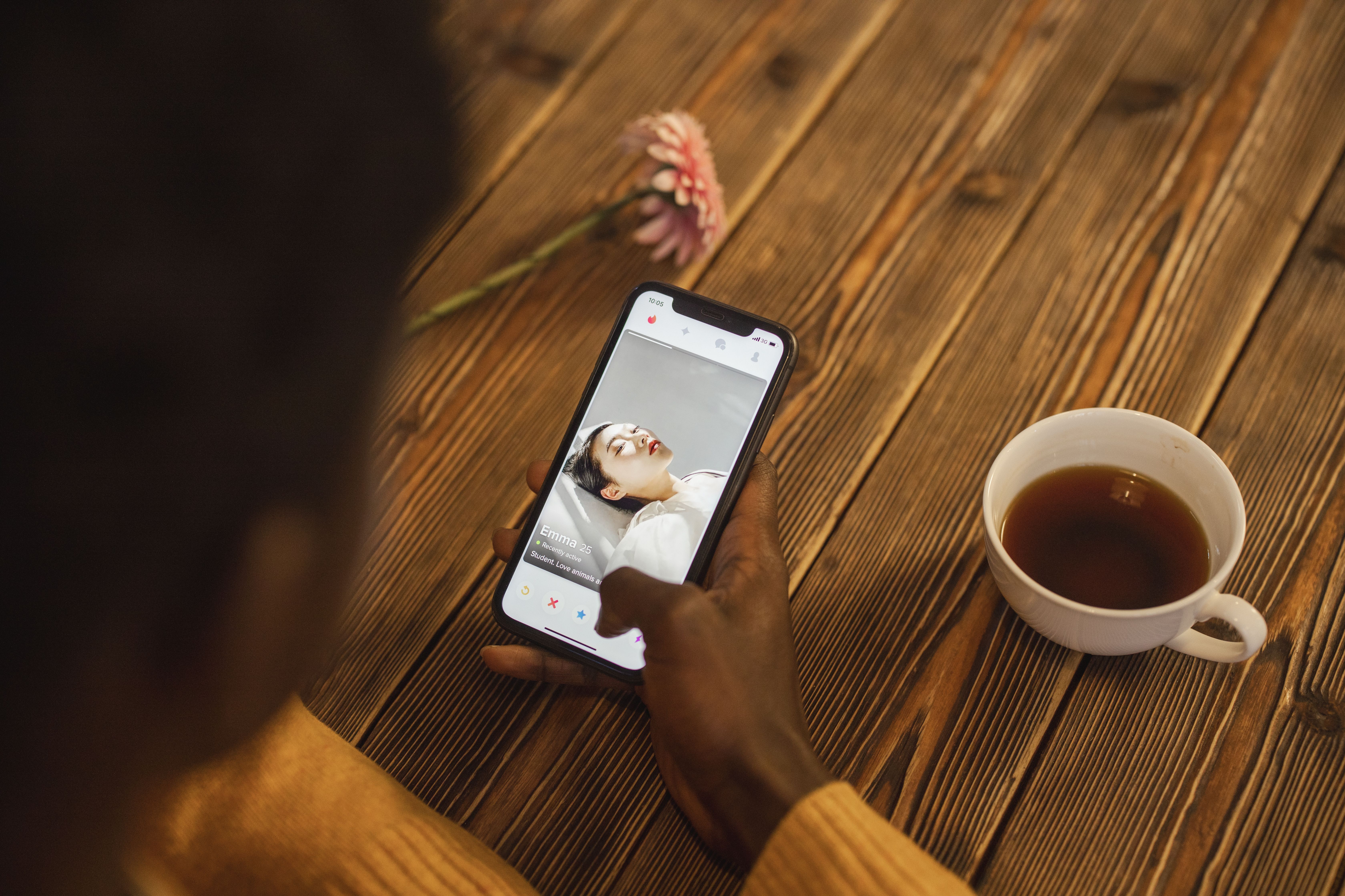 Person browsing a dating app on a smartphone with a cup of tea nearby