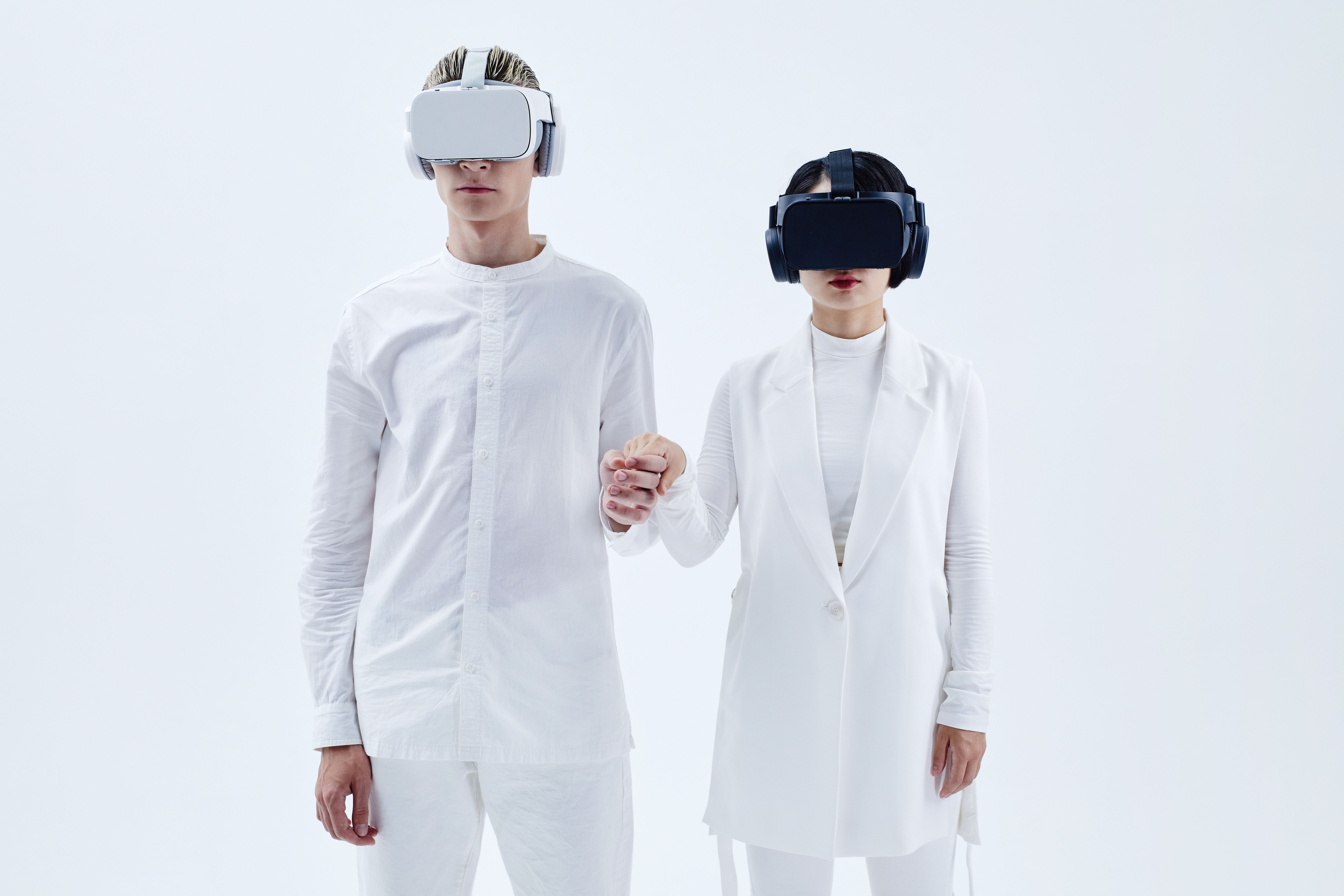 Two people wearing VR headsets and holding hands while immersed in virtual reality
