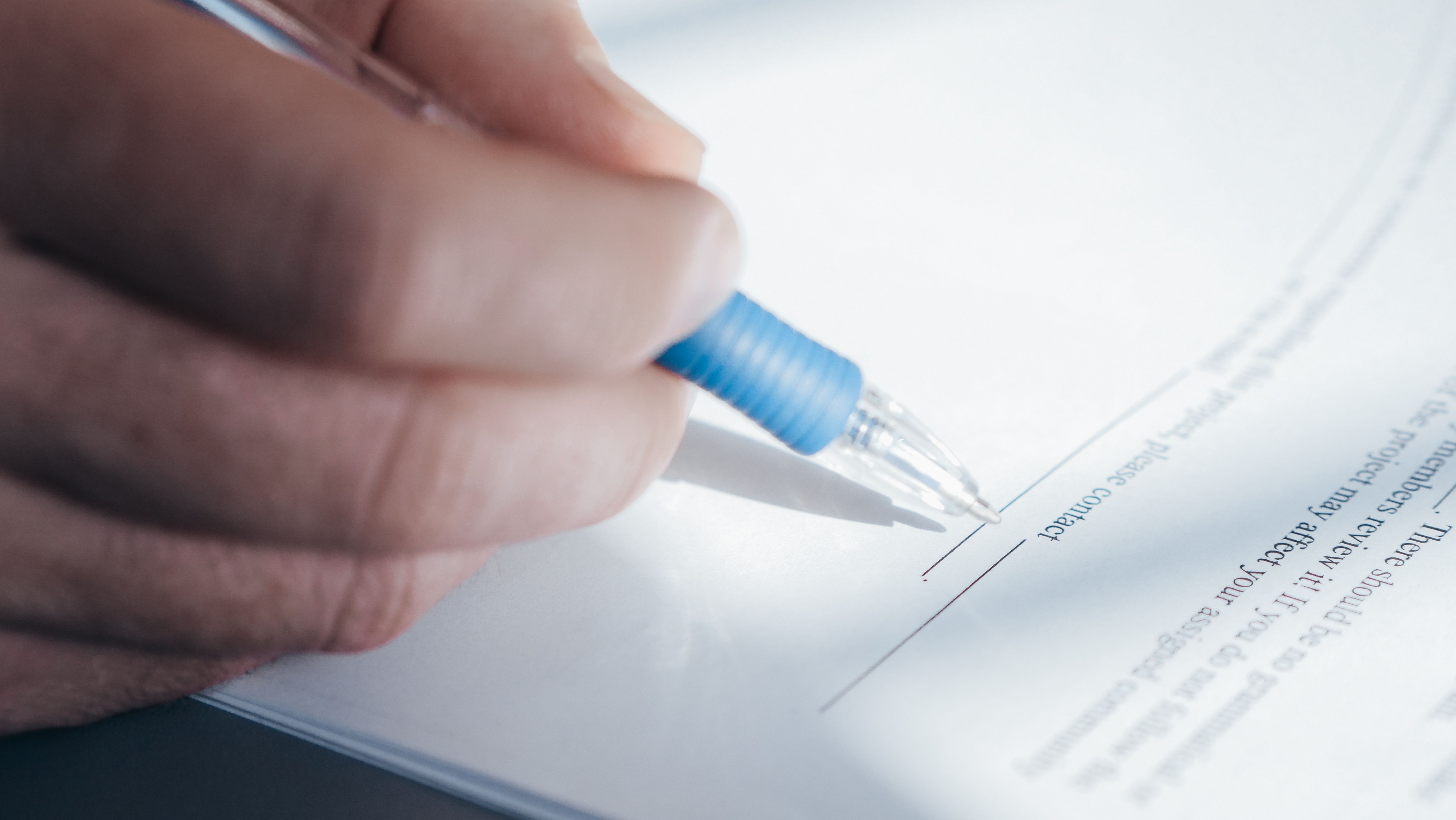 Close-up of a hand holding a pen while signing a formal consumer claim document