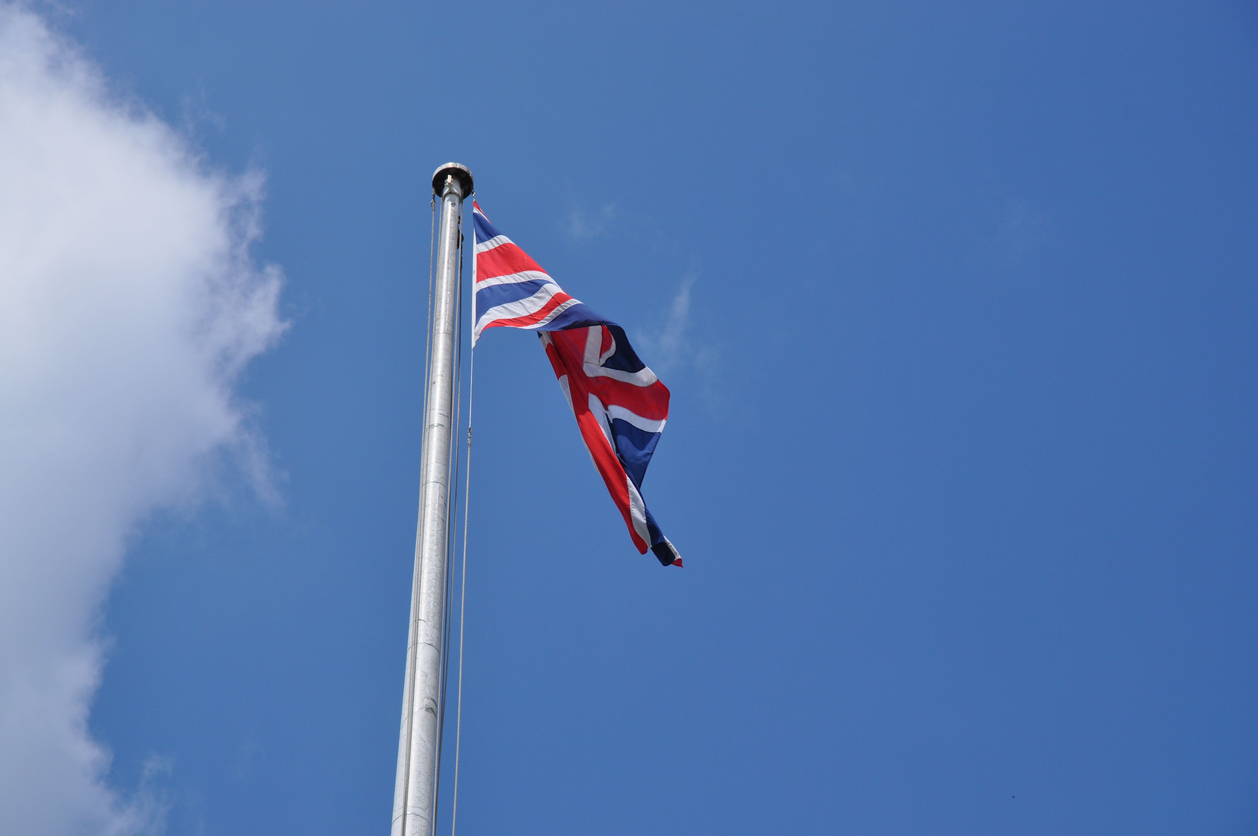 Union Jack flag waving on a flagpole against a clear blue sky in London, UK